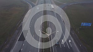 Aerial shot. Cars driving by the road. Transport interchange. Cars ride under and above the bridge. Thick fog.