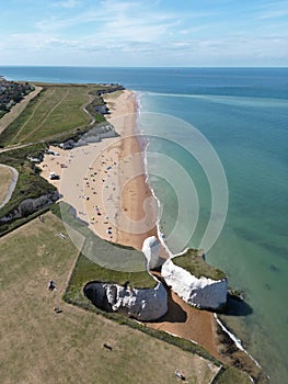 Aerial shot of coastal cliffs and sandy beach surrounded by greenish-blue waters. Broadstairs, UK.