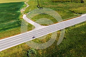 Aerial shot of cyclist riding his bicycle along the asphalt road through countryside on sunny summer day, drone pov