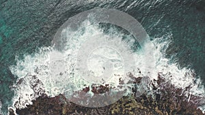 Aerial shot from drone. Top view on the rocky ocean shore. Blue Waves of the Pacific Ocean is crashing on the rock