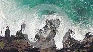 Aerial shot from drone. Top view on the rocky ocean shore. Blue Waves of the Pacific Ocean is crashing on the rock