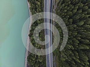 Aerial shot of an empty road in the middle of a fir forest alongside a sea