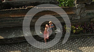 Aerial shot of the family travelers sitting in a stairs of the Pura Gunung Lebah temple in Ubud on the Bali island