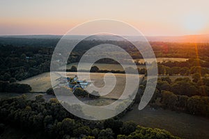 Aerial shot of farmland and house surrounded by woodland in Surrey, UK. Sunset