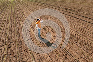 Aerial shot of female farmer standing in corn sprout field and examining crops.