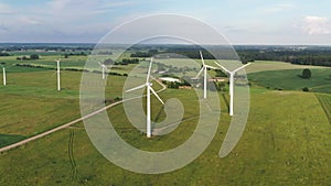 Aerial shot flying towards rotating wind turbines in green field