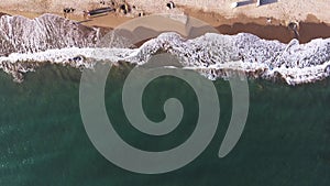 Aerial shot of foamy waves gently crashing onto a sandy shore, depicting the tranquil interface of ocean and land, Costa