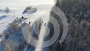 Aerial shot following car driving through rural area in snow covered winter