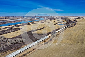 Aerial shot of a freight train passing through a wide field alongside the South Saskatchewan River