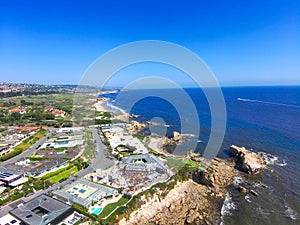 An aerial shot of a gorgeous summer landscape at the beach with blue ocean water and waves crashing into the large rocks