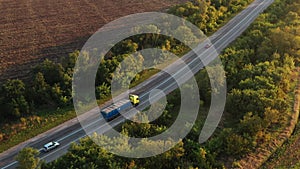 Aerial shot of a grain truck driving on the road in beautiful countryside in the summer sunset. Drone view of lorry