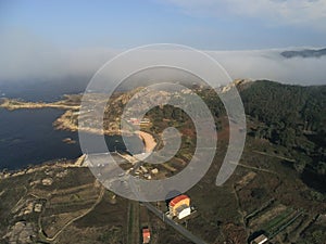 Aerial shot of grassy fields near the sea under a foggy sky in Galicia, Spain