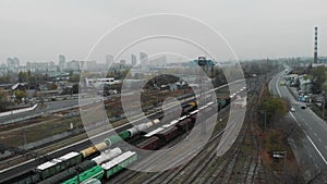 Aerial shot of industrial city and cargo freight train moving along the street with wagons filled with goods and fuel tanks