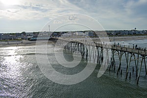 aerial shot of the Kure Beach Pier with ocean water, waves, people on the pier and relaxing in the sand on the beach with homes