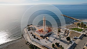 an aerial shot of a lighthouse on the shore with blue water