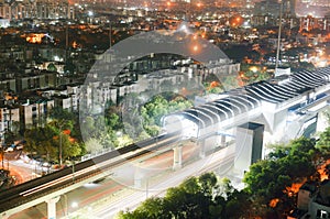 Aerial shot of lit metro sation with trails from leaving train and traffic