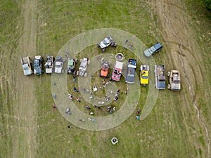 Aerial shot of lots of people near off-road vehicles in a grass field near trees