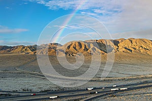 an aerial shot of majestic mountain ranges in the desert with cars and trucks driving on the highway, blue sky, clouds and a photo