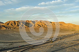 an aerial shot of majestic mountain ranges in the desert at sunset with cars and trucks driving on the highway in Yermo California