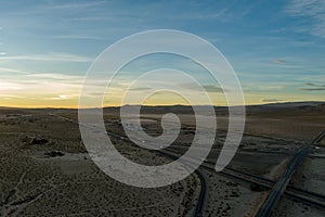 an aerial shot of majestic mountain ranges in the desert at sunset with cars and trucks driving on the highway in Yermo California