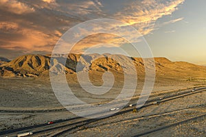 an aerial shot of majestic mountain ranges in the desert at sunset with cars and trucks driving on the highway in Yermo California photo