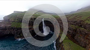 Aerial shot of Mulafossur waterfall and a cliffed coast in Vagar, Faroe Islands