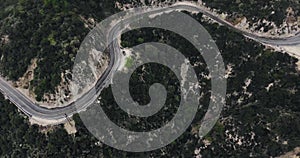 Aerial shot of a parked black car on the side of a winding road in wooded mountains