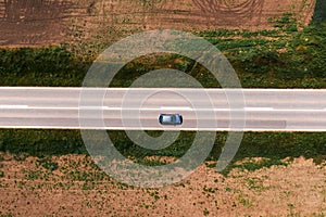 Aerial shot of passenger car driving along asphalt road through countryside landscape with no trees and shade on hot sunny summer