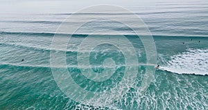 Aerial shot of people surfboarding and swimming in the calm waters of the blue ocean