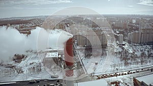 Aerial shot of a power plant smokestack in urban residential area in winter