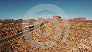 Aerial shot of red cargo truck moving along desert highway road with amazing mountain skyline in Monument Valley, USA.