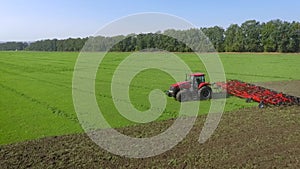 Aerial shot of red tractor plowing agricultural field in summer