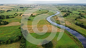 Aerial shot of a river surrounded by green field in summer, Tykocin, Poland