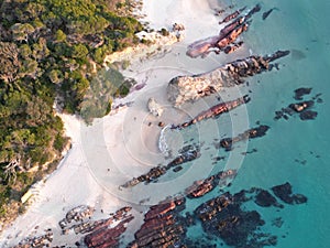 Aerial shot of rocks on the sandy beach with crystal clear water in Merimbula, Australia.