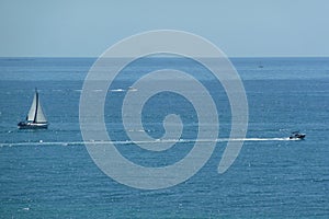 Aerial shot of a sailboat and a high-speed boat in blue sea under clear sky