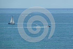 Aerial shot of a sailboat and a high-speed boat in blue sea under clear sky