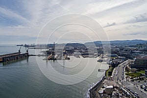 aerial shot of the San Francisco Bay with ships docked, cranes, rippling ocean water, buildings and cars driving on the street