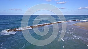 Aerial shot of sandy beach and Sea waves wash rough stones at break wall.