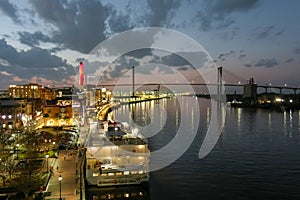 aerial shot of the Savannah River at sunset with the Talmadge Memorial Bridge, ships docked along the banks with restaurants