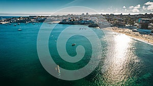 Aerial shot of a sea reflecting sunshine with a cityscape in the background