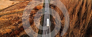 Aerial shot of semi truck and car driving along the highway through autumn scenery landscape, drone pov