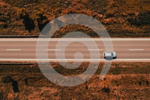 Aerial shot of single gray car driving down the road through countryside in late summer