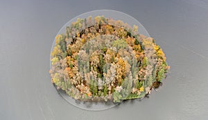 Aerial shot of a small island  covered in colorful trees and surrounded by the lake in Estonia