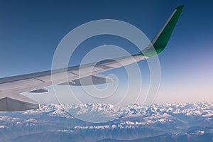 Aerial shot of the snow-capped mountains with an airplane green winglet on the foreground