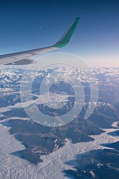 Aerial shot of the snow-capped mountains with an airplane green winglet on the foreground