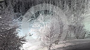 Aerial shot of snowboarders moving down the ski-run at night. Snowfields and forest in the distance. Doing winter sports