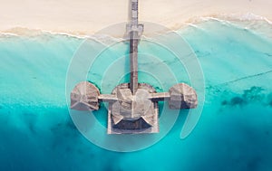 Aerial shot of the Stilt hut with palm thatch roof washed with turquoise Indian ocean waves on the white sand sandbank beach on