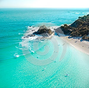 Aerial shot at sunrise over the ocean and white sand beach with swimmers and surfers enjoying summer