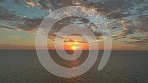 An Aerial Shot with Sunset and Beautiful Cloudy Sky flying into the Ocean with Clear Horizon and a Person Surfing