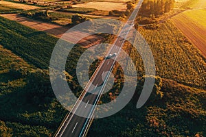 Aerial shot of traffic on countryside road in summer sunset, high angle view drone pov image of cars driving along the highway